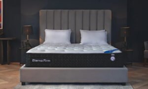 Celeste Eterna Firm mattress in a modern bedroom with gray headboard, white bedding, and black side panel featuring tufted design and certification badge.
